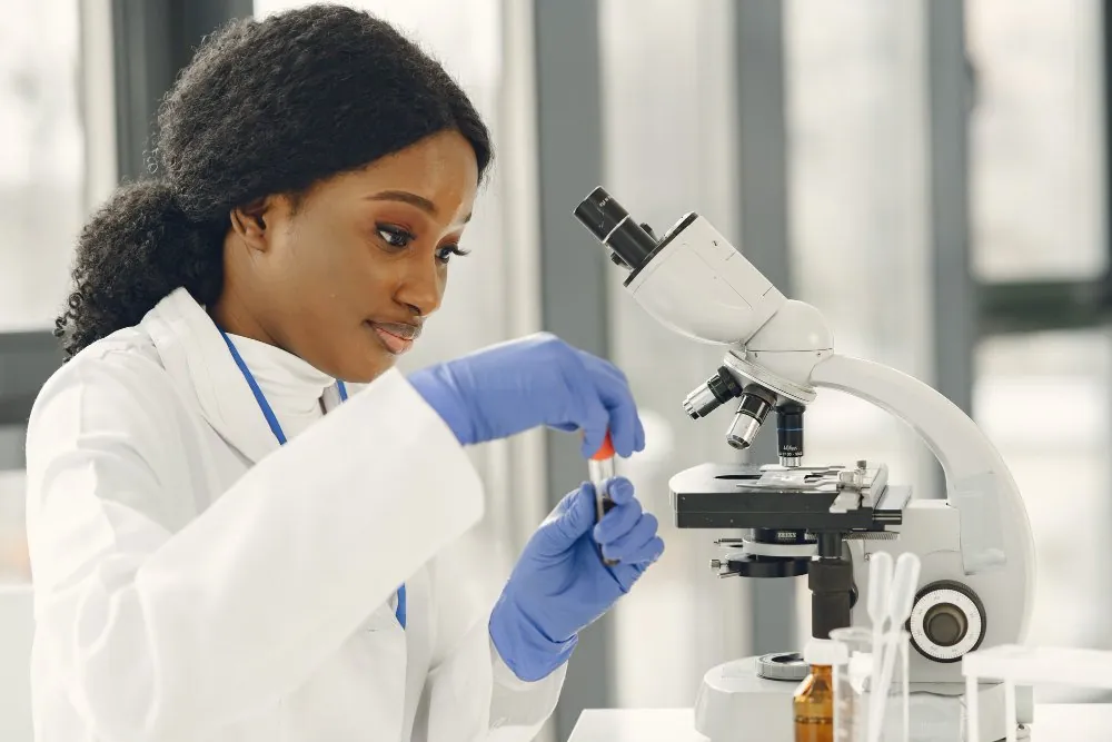 Chercheuse en blouse observant un échantillon au microscope dans un laboratoire